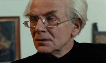 Movie still from “The American Friend” (1977), directed by Wim Wenders – An older man wearing glasses and a black shirt; Close Up shot, Over the shoulder angle