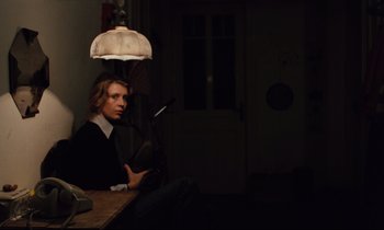 Movie still from “The American Friend” (1977), directed by Wim Wenders – A man sitting at a table in a dark room; Medium shot, Over the shoulder angle