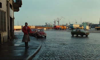 Movie still from “The American Friend” (1977), directed by Wim Wenders – A woman standing on the side of a road in the rain; Wide shot, Low angle