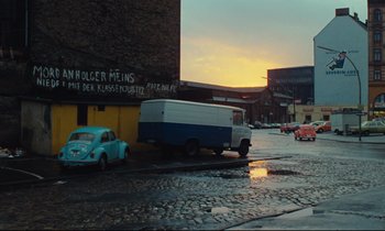 Movie still from “The American Friend” (1977), directed by Wim Wenders – A van parked on the side of the road near a building; Extreme Wide shot, High angle