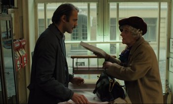 Movie still from “The American Friend” (1977), directed by Wim Wenders – A man and a woman are looking at a book together; Medium shot, Low angle