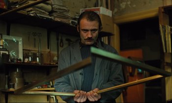 Movie still from “The American Friend” (1977), directed by Wim Wenders – A man holding a pair of sticks in his hands; Medium shot, Low angle