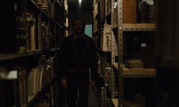 Movie still from “The American Friend” (1977), directed by Wim Wenders – A man standing in a room full of books; Medium shot, Low angle