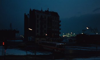 Movie still from “The American Friend” (1977), directed by Wim Wenders – A train is traveling down the tracks near a building; Extreme Wide shot, Low angle