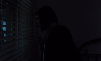 Movie still from “The American Friend” (1977), directed by Wim Wenders – A man standing in front of a window at night; Medium shot, Low angle