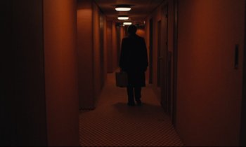 Movie still from “The American Friend” (1977), directed by Wim Wenders – A person walking down a hallway with a suitcase; Wide shot, High angle