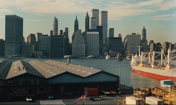 Movie still from “The American Friend” (1977), directed by Wim Wenders – A view of a city from a pier with a boat in the water; Extreme Wide shot, High angle