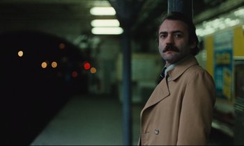 Movie still from “The American Friend” (1977), directed by Wim Wenders – A man standing next to a pole in a train station; Close Up shot, Low angle