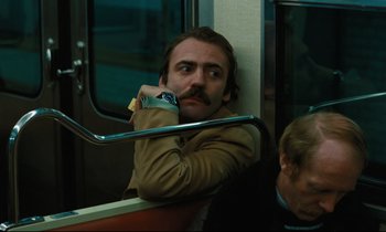 Movie still from “The American Friend” (1977), directed by Wim Wenders – A man sitting on a train with his hand on his chin; Medium shot, Low angle