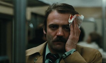 Movie still from “The American Friend” (1977), directed by Wim Wenders – A man holding a piece of pizza in front of his face; Close Up shot, High angle