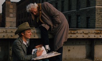 Movie still from “The American Friend” (1977), directed by Wim Wenders – An old woman standing next to an older man; Medium shot, Low angle