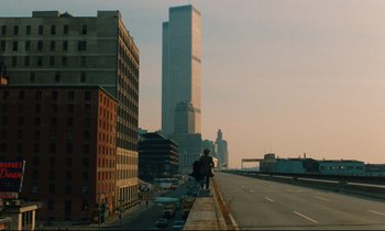 Movie still from “The American Friend” (1977), directed by Wim Wenders – A view of a city street with tall skyscrapers in the background; Extreme Wide shot, High angle