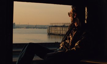 Movie still from “The American Friend” (1977), directed by Wim Wenders – A man sitting on a bench looking out at the water; Medium shot, Low angle