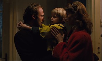 Movie still from “The American Friend” (1977), directed by Wim Wenders – A man and a woman holding a young boy; Medium shot, Low angle