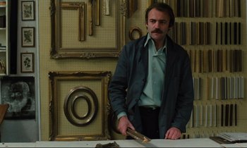 Movie still from “The American Friend” (1977), directed by Wim Wenders – A man cutting a piece of wood with a large knife; Medium shot, Low angle