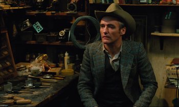 Movie still from “The American Friend” (1977), directed by Wim Wenders – A man wearing a cowboy hat sitting in front of a table; Medium shot, Low angle