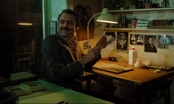 Movie still from “The American Friend” (1977), directed by Wim Wenders – A man sitting at a table with a lamp in front of him; Medium shot, Low angle
