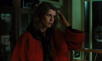 Movie still from “The American Friend” (1977), directed by Wim Wenders – A woman in a red coat is holding her hand up to her head; Medium shot, Low angle