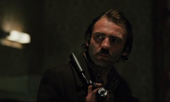 Movie still from “The American Friend” (1977), directed by Wim Wenders – A man holding a gun in his hand and looking at the camera; Close Up shot, Low angle