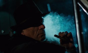 Movie still from “The American Friend” (1977), directed by Wim Wenders – A man in a black hat smoking a cigarette and holding a cell phone; Close Up shot, Low angle