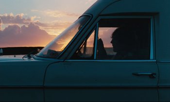 Movie still from “The American Friend” (1977), directed by Wim Wenders – A person sitting in the driver's seat of a car; Wide shot, Low angle