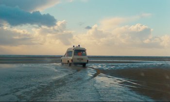 Movie still from “The American Friend” (1977), directed by Wim Wenders – An ambulance driving down a flooded road near the ocean; Extreme Wide shot, Low angle