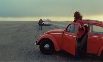 Movie still from “The American Friend” (1977), directed by Wim Wenders – A woman standing next to an orange car; Wide shot, High angle