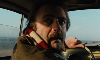 Movie still from “The American Friend” (1977), directed by Wim Wenders – A person in a car wearing a scarf; Close Up shot, Low angle