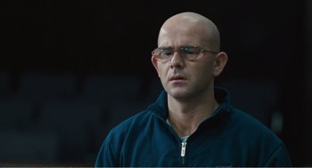 Movie still from “The Angels' Share” (2012), directed by Ken Loach – A bald man wearing glasses and a blue jacket; Close Up shot, Low angle
