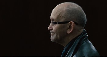Movie still from “The Angels' Share” (2012), directed by Ken Loach – An older bald man with glasses looking to his left; Close Up shot, Over the shoulder angle