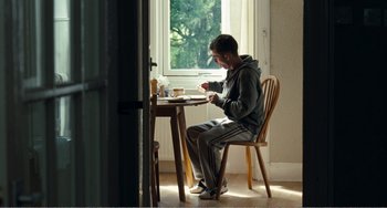 Movie still from “The Angels' Share” (2012), directed by Ken Loach – A man sitting at a table in front of a cup of coffee; Wide shot, Low angle