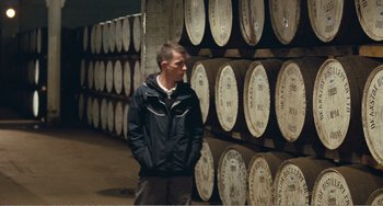 Movie still from “The Angels' Share” (2012), directed by Ken Loach – A man standing in front of a bunch of barrels; Wide shot, Over the shoulder angle