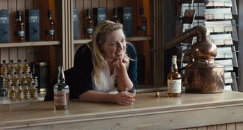 Movie still from “The Angels' Share” (2012), directed by Ken Loach – A woman sitting at a table with a glass of whiskey; Medium shot, Over the shoulder angle