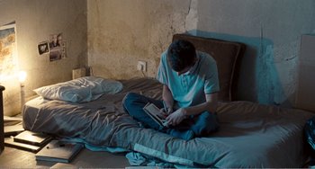 Movie still from “The Angels' Share” (2012), directed by Ken Loach – A man sitting on top of a bed using a laptop; Medium shot, High angle
