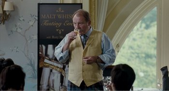 Movie still from “The Angels' Share” (2012), directed by Ken Loach – A man in a yellow vest is eating something; Medium shot, Over the shoulder angle