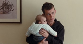 Movie still from “The Angels' Share” (2012), directed by Ken Loach – A man holding a baby in his arms; Medium shot, Over the shoulder angle