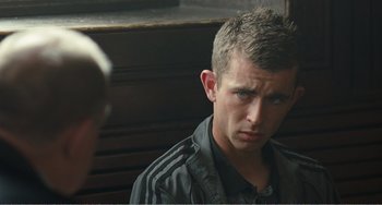 Movie still from “The Angels' Share” (2012), directed by Ken Loach – A young man in a black jacket is looking at the camera; Close Up shot, Over the shoulder angle