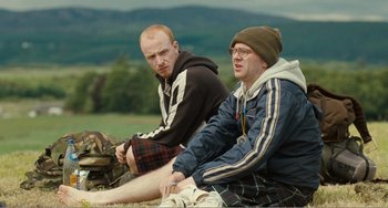 Movie still from “The Angels' Share” (2012), directed by Ken Loach – A couple of men sitting next to each other on a field; Medium shot, Over the shoulder angle