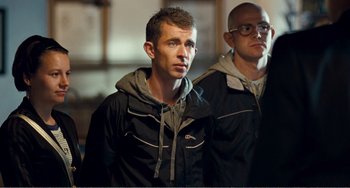 Movie still from “The Angels' Share” (2012), directed by Ken Loach – A man standing next to another man wearing glasses; Medium shot, Over the shoulder angle