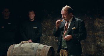 Movie still from “The Angels' Share” (2012), directed by Ken Loach – A man in a suit sniffs a piece of food; Medium shot, Over the shoulder angle