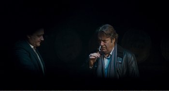 Movie still from “The Angels' Share” (2012), directed by Ken Loach – A man looking at a cell phone while standing next to another man; Medium shot, Over the shoulder angle