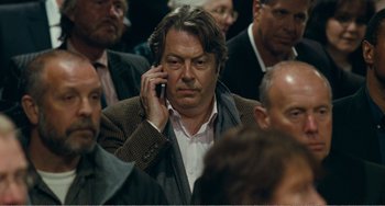 Movie still from “The Angels' Share” (2012), directed by Ken Loach – A man is talking on a cell phone while sitting in a crowd of people; Close Up shot, Over the shoulder angle
