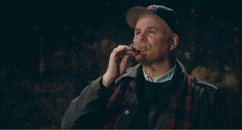 Movie still from “The Angels' Share” (2012), directed by Ken Loach – A man in a baseball cap is drinking from a straw; Medium shot, Over the shoulder angle