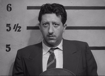 Movie still from “The Asphalt Jungle” (1950), directed by John Huston – Black and white photograph of a man in a suit and tie in front of a wall; Medium shot, Low angle