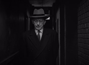 Movie still from “The Asphalt Jungle” (1950), directed by John Huston – An older man in a suit and hat in a hallway; Medium shot, Low angle