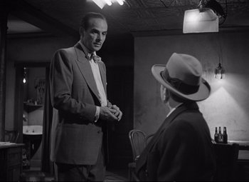 Movie still from “The Asphalt Jungle” (1950), directed by John Huston – A man wearing a suit and tie talking to another man wearing a hat; Medium shot, Over the shoulder angle