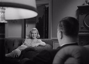Movie still from “The Asphalt Jungle” (1950), directed by John Huston – A woman sitting on top of a couch next to a man; Medium shot, Over the shoulder angle