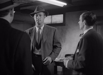 Movie still from “The Asphalt Jungle” (1950), directed by John Huston – A man in a suit and hat standing next to another man in a suit; Medium shot, Over the shoulder angle