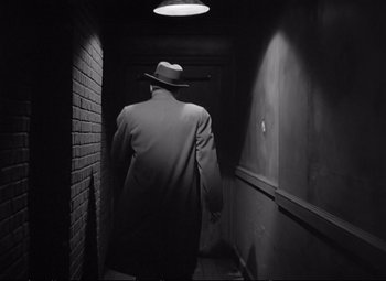 Movie still from “The Asphalt Jungle” (1950), directed by John Huston – A man wearing a hat walking down a dark hallway; Medium shot, Low angle