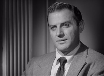 Movie still from “The Asphalt Jungle” (1950), directed by John Huston – A man wearing a suit and tie in front of a wall; Close Up shot, Low angle